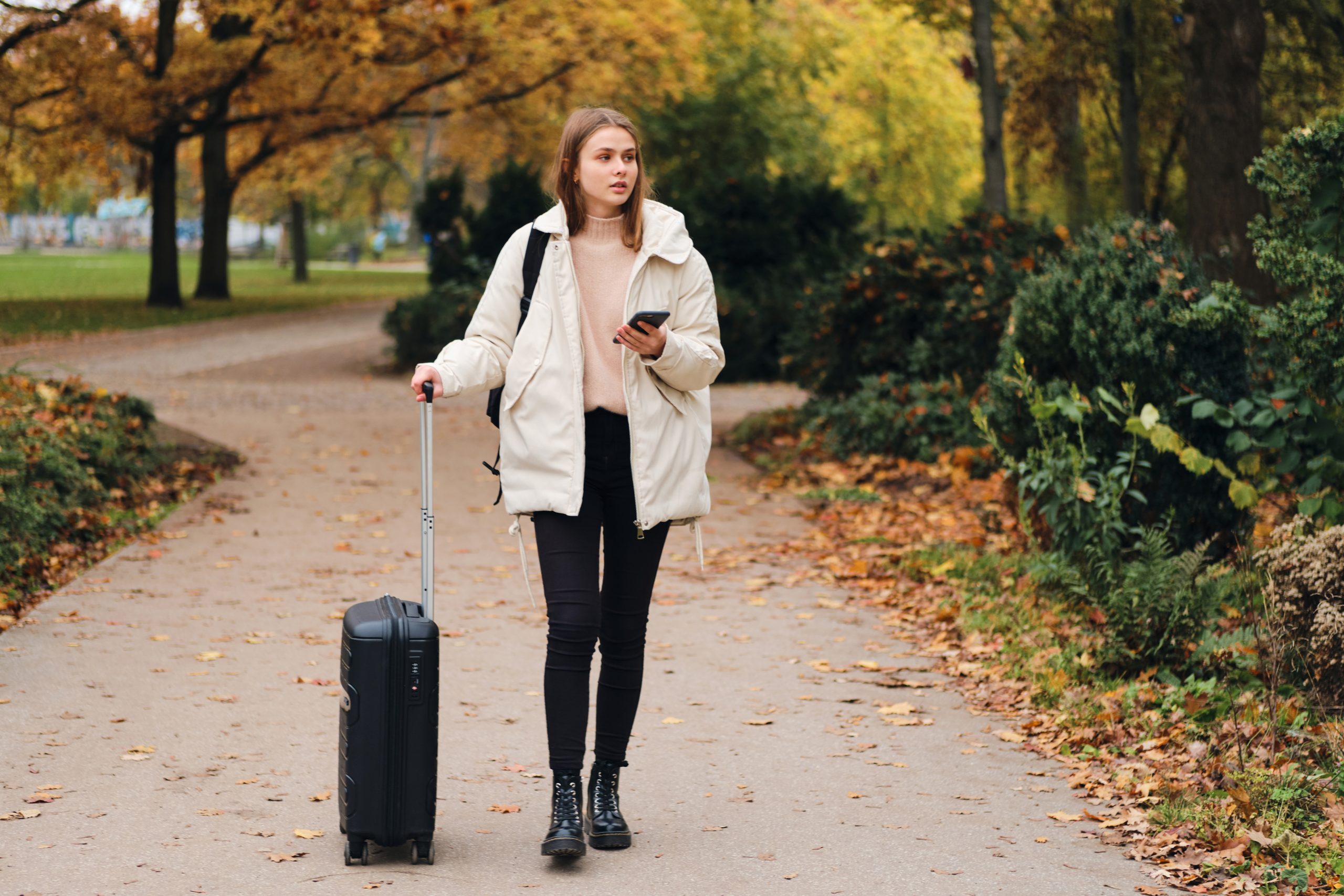 Attractive casual girl in down jacket with suitcase and cellphon